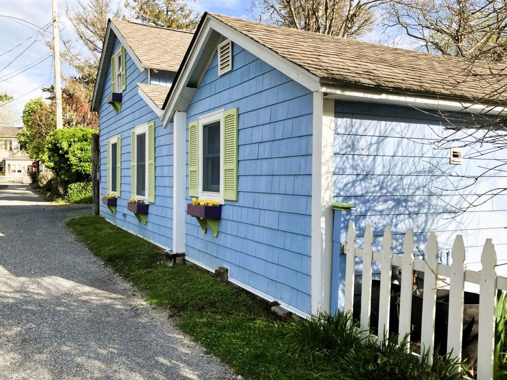 Side of blue cottage with green shutters along Golf Lane with purple window boxes filled with flowers